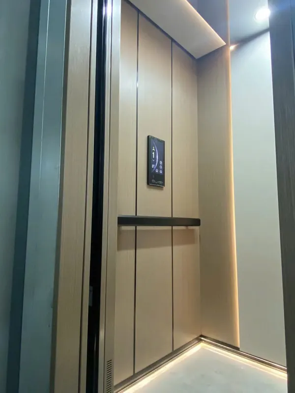 Cabin thang máy vách ốp tấm màu be, đèn LED hắt viền, tay vịn đen