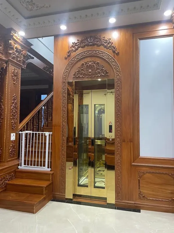 Thang máy gia đình lắp đặt thực tế, khung ốp gỗ chạm khắc cạnh cầu thang gỗ